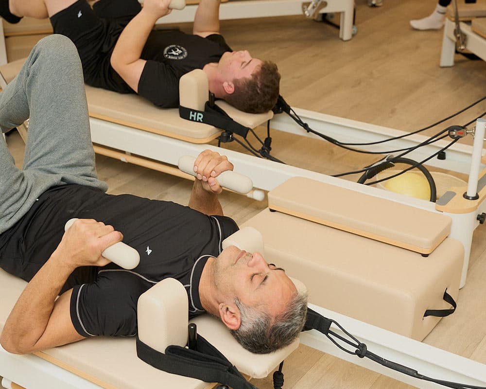 Two men lying back on adjacent reformers mid-exercise